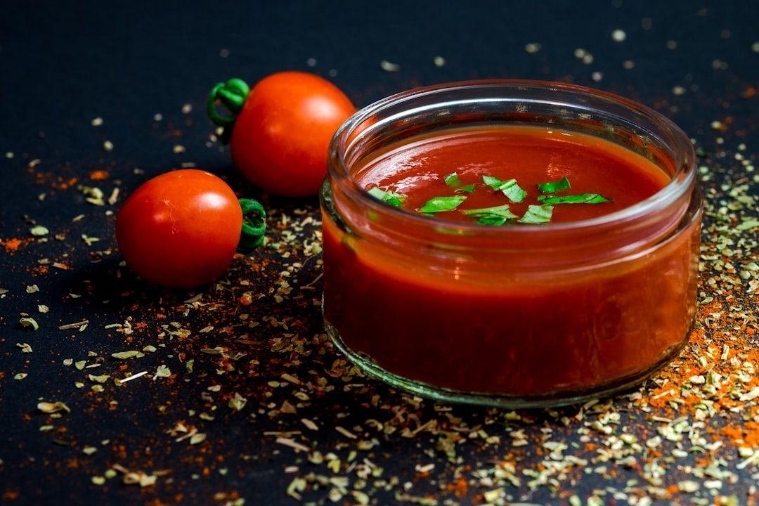 Glasburk med röd tomatsås, toppad med gröna örter och tomater bredvid